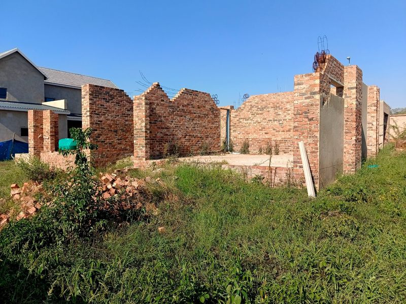 An unfinished residential construction site showing exposed brick walls and a concrete foundation slab, currently in the early stages of development.