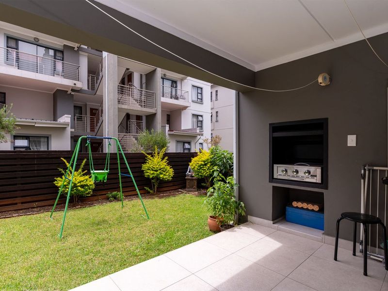 A covered patio area featuring a built-in braai, tiled flooring, and direct access to a private garden space.