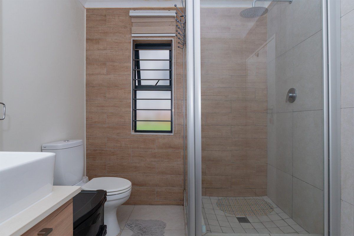Modern bathroom featuring a glass-enclosed shower with a rain shower head, a vanity basin, and neutral-toned wall tiling.