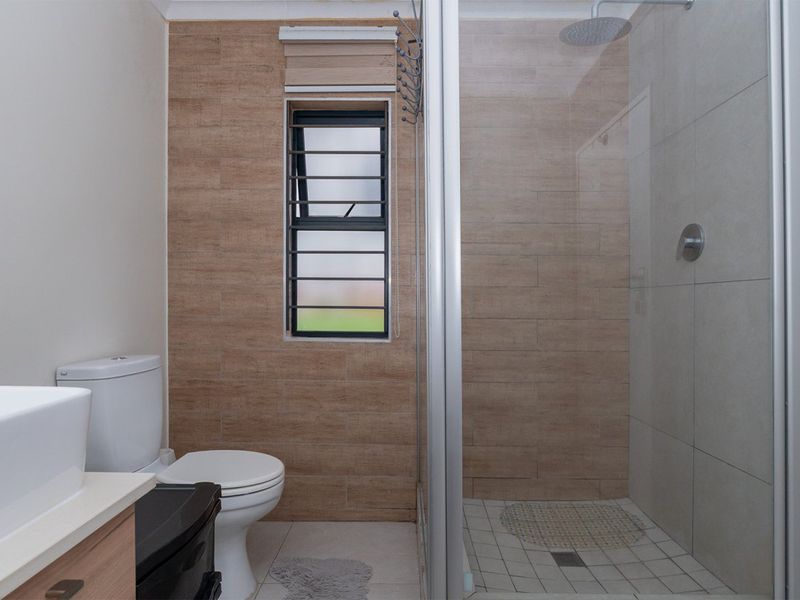 Modern bathroom featuring a glass-enclosed shower with a rain shower head, a vanity basin, and neutral-toned wall tiling.