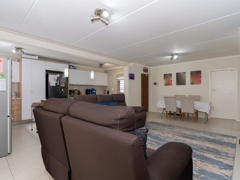 Spacious open-plan living and dining area featuring tiled floors, neutral walls, and a functional kitchen with built-in cabinetry.