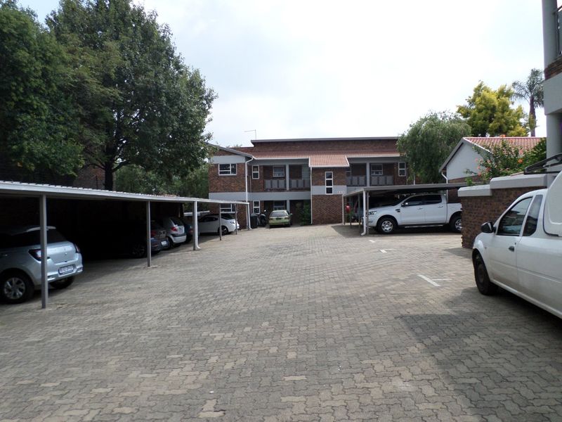 Exterior view of the apartment complex featuring a paved parking area with covered carports and brick building facades.