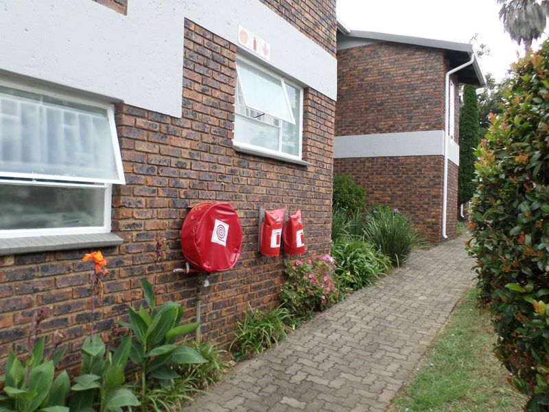 Exterior view of the apartment building featuring face brick walls, a paved walkway, and installed fire safety equipment including a hose reel and extinguishers.