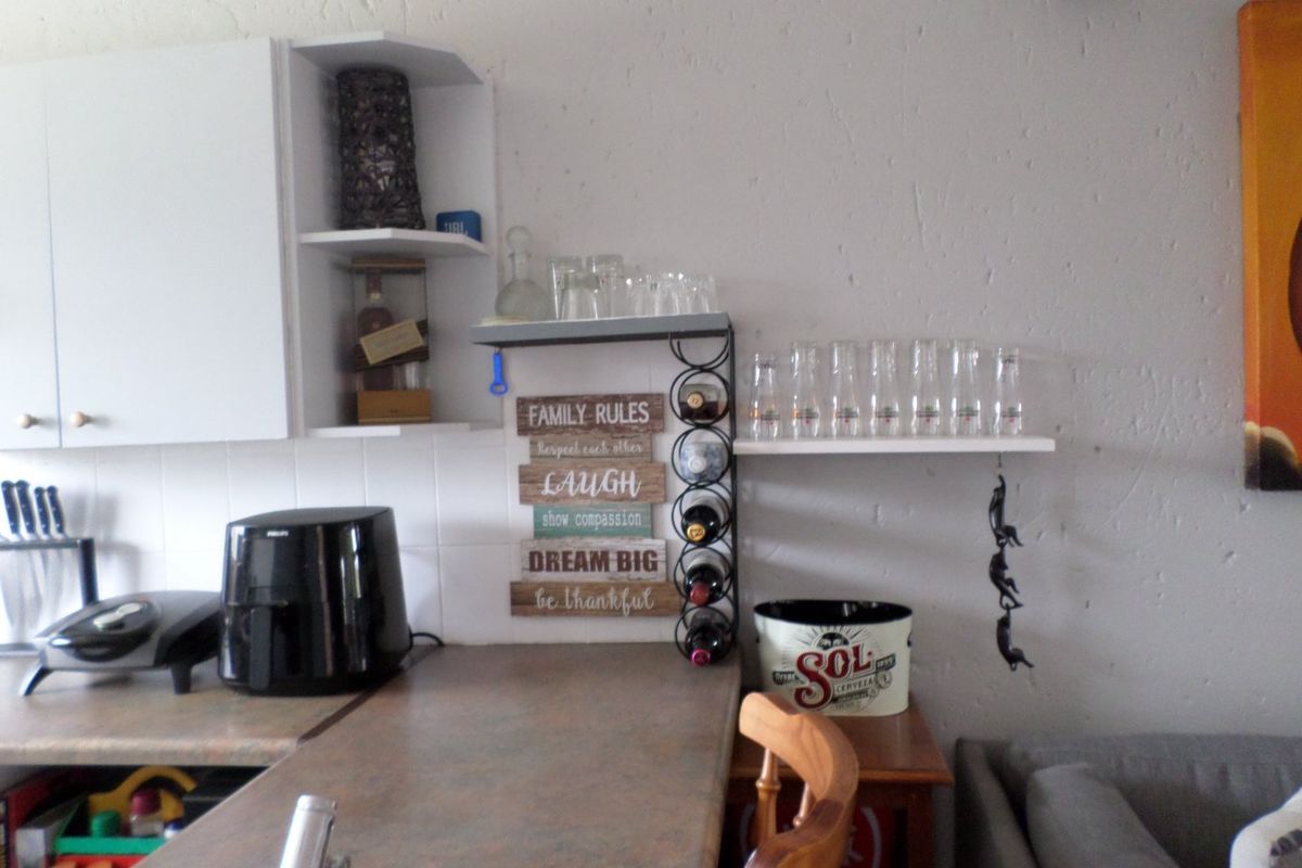 A kitchen area featuring laminate countertops, tiled backsplash, and wall-mounted shelving units providing additional storage space.