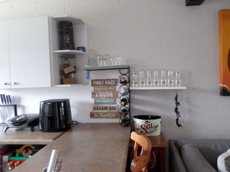 A kitchen area featuring laminate countertops, tiled backsplash, and wall-mounted shelving units providing additional storage space.