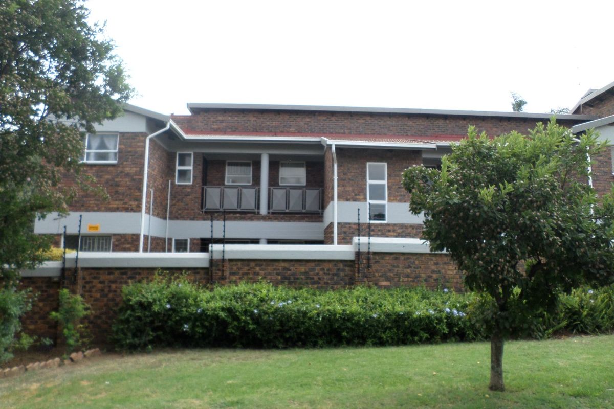 Exterior view of a face brick apartment building featuring balconies with metal balustrades, secured by a perimeter wall with electric fencing.