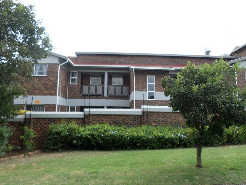 Exterior view of a face brick apartment building featuring balconies with metal balustrades, secured by a perimeter wall with electric fencing.