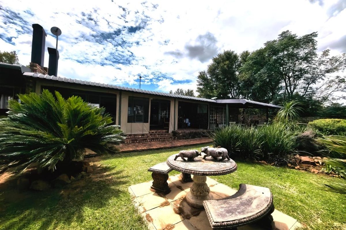 Rear view of the property featuring a covered patio area, brick paving, and a well-maintained garden with mature landscaping.
