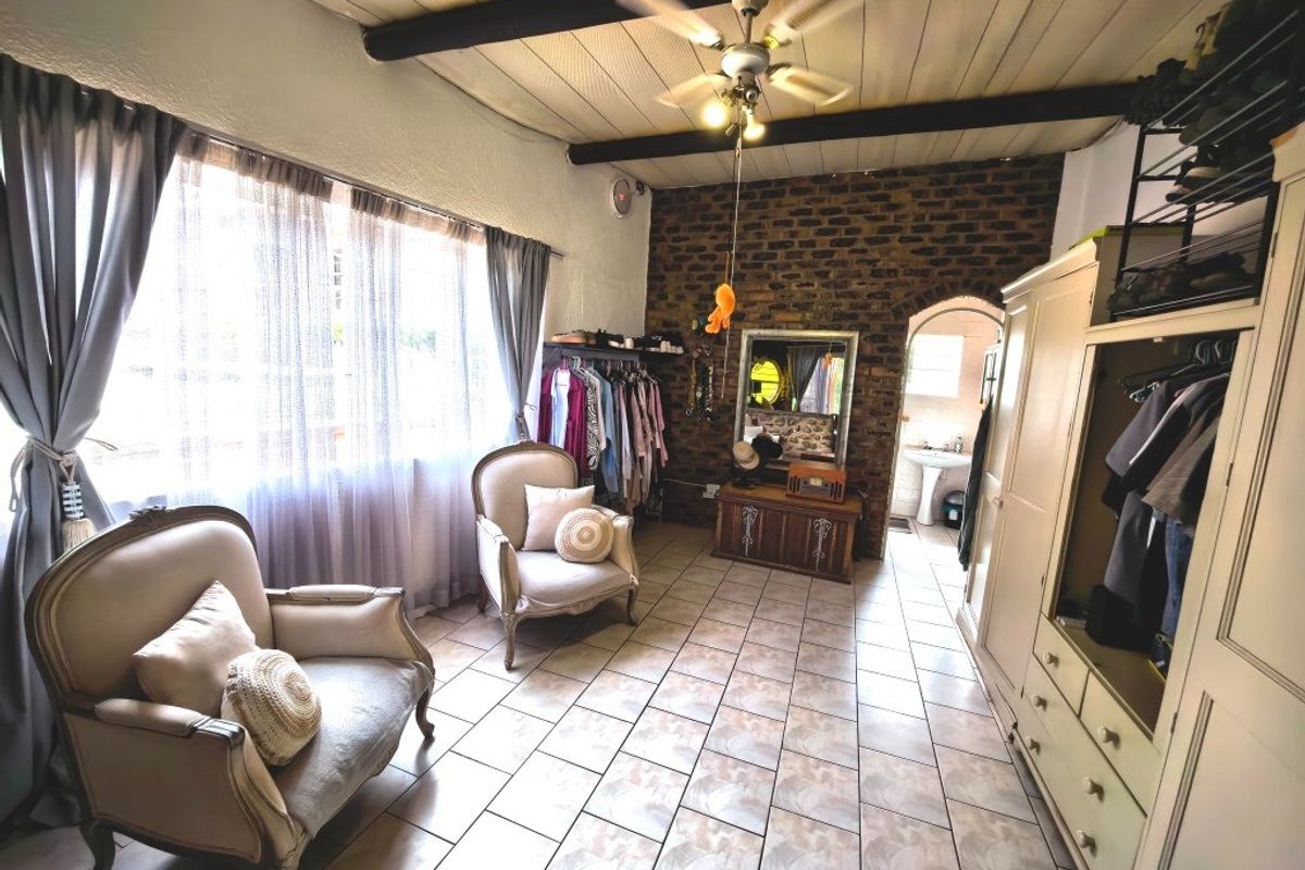 A bedroom featuring exposed brick walls, timber ceiling beams, and tiled flooring, with an arched doorway leading to an adjoining space.