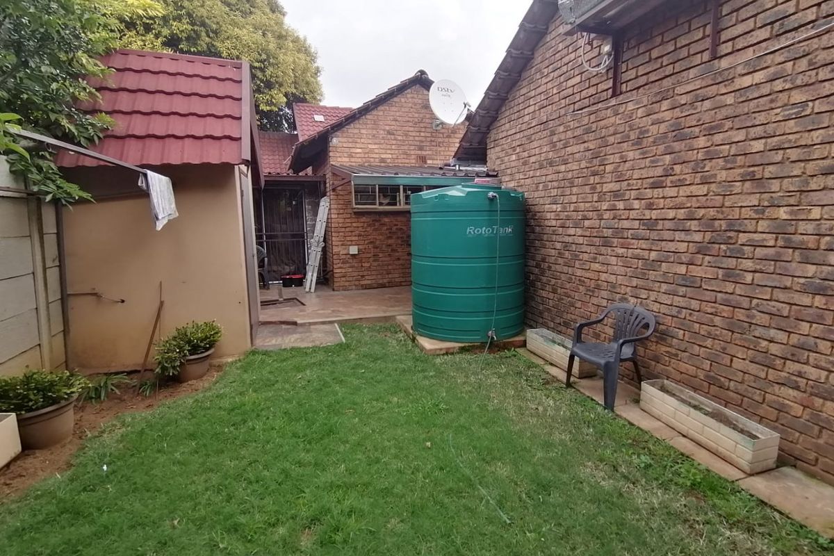 Rear garden area featuring a brick exterior, water storage tank, solar water heating system, and paved access path.