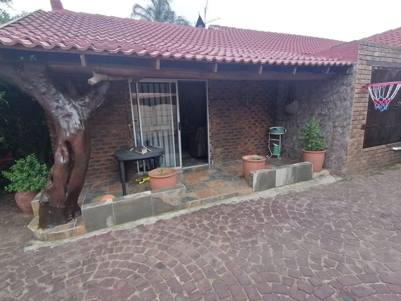 A covered patio area featuring brick walls, tiled flooring, and a sliding glass door entrance, providing a functional outdoor space for relaxation.