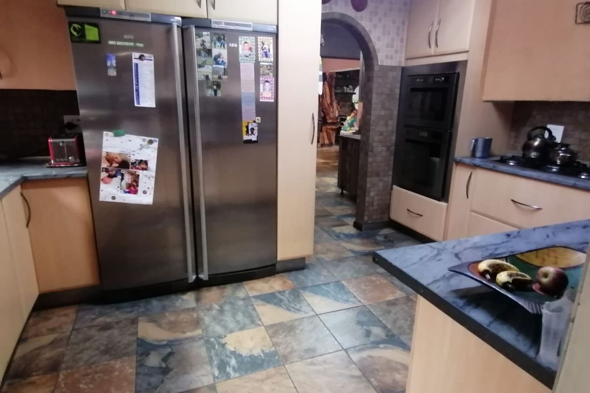 A functional kitchen featuring built-in cabinetry, a double oven, gas hob, and durable tiled flooring with an arched transition to the adjacent living space.