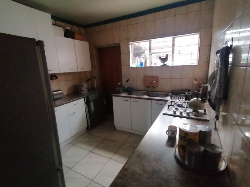 A functional kitchen featuring white cabinetry, a gas hob, double sink, and tiled finishes. The space offers a practical layout with potential for modernization.