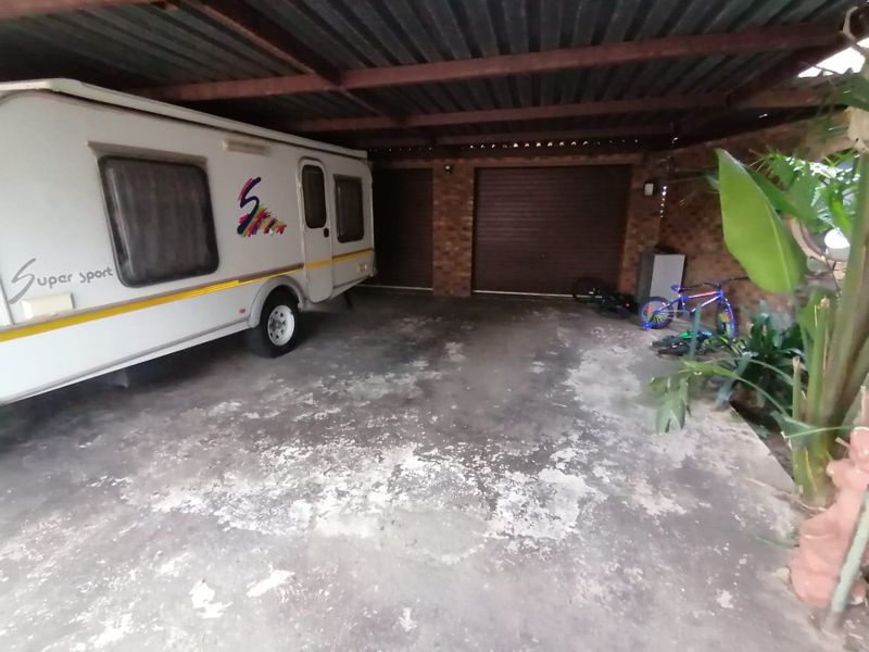 A covered double garage area featuring exposed brick walls, corrugated metal roofing, and a concrete floor with visible surface wear.