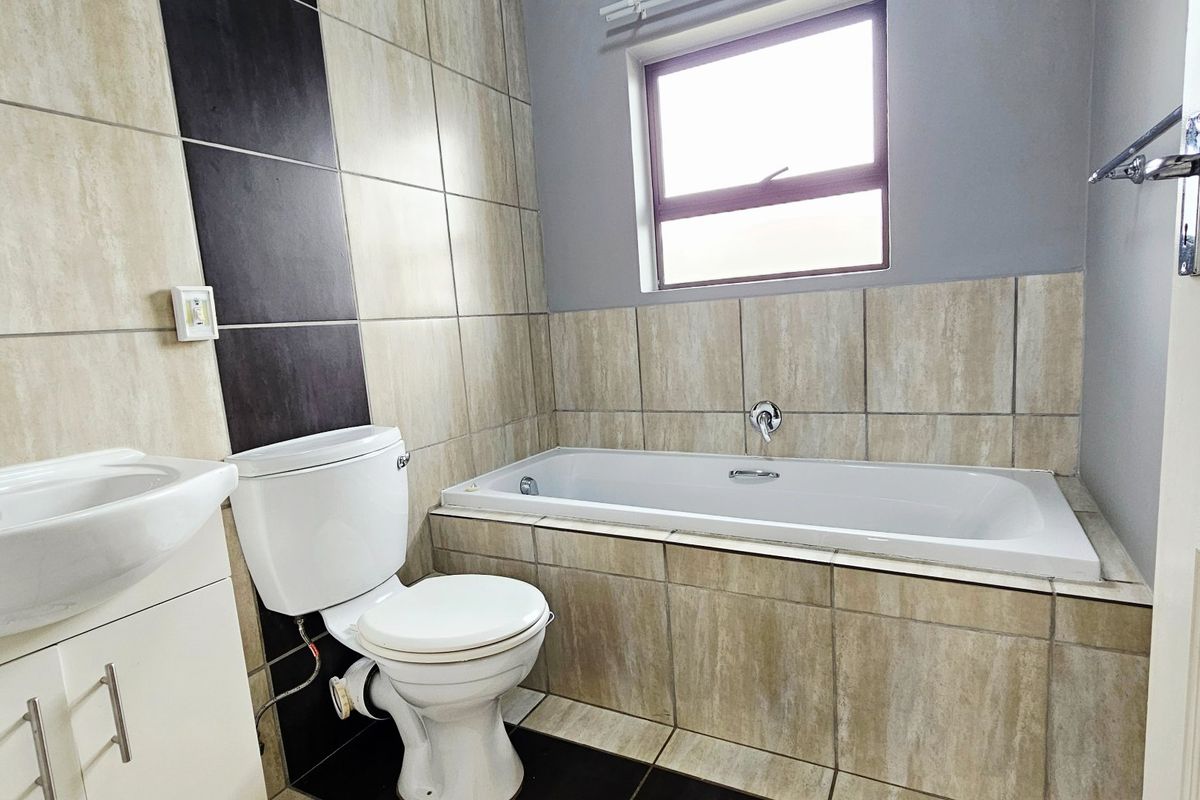 A clean, modern bathroom featuring a built-in bathtub, vanity with basin, and neutral-toned wall and floor tiling.