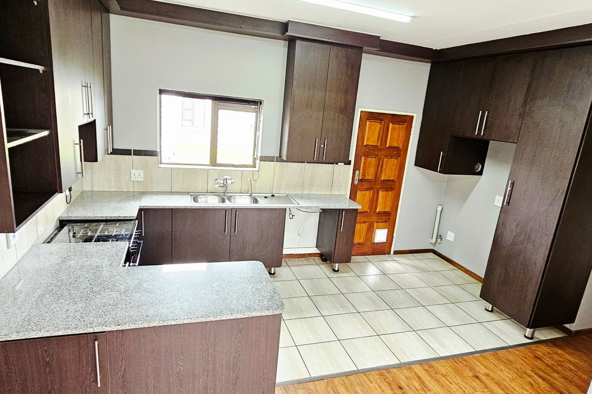 A clean, functional kitchen featuring dark wood cabinetry, granite countertops, a double basin sink, and tiled flooring with direct exterior access.
