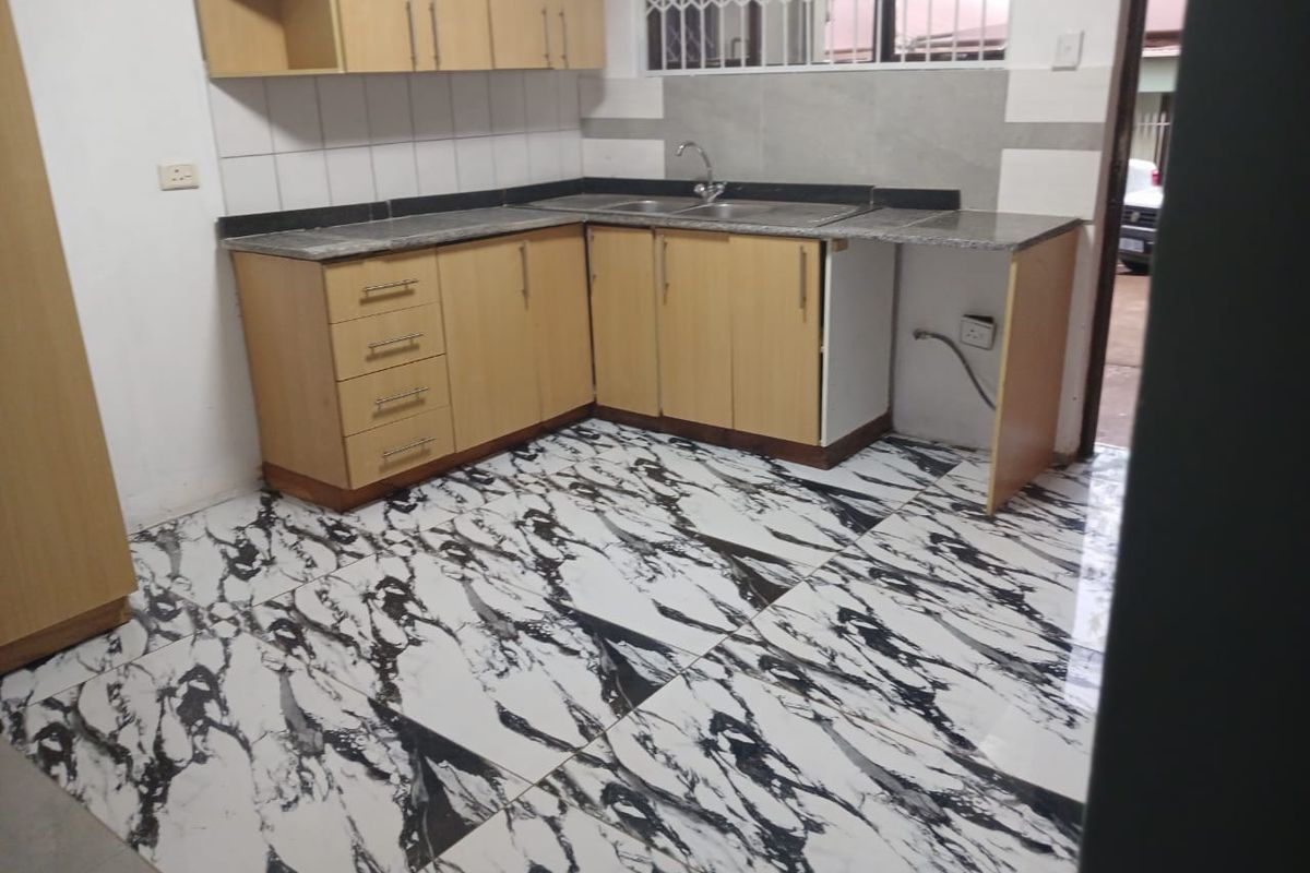 A functional kitchen featuring light wood cabinetry, granite countertops, and striking marble-effect floor tiles, offering a clean and modern aesthetic.