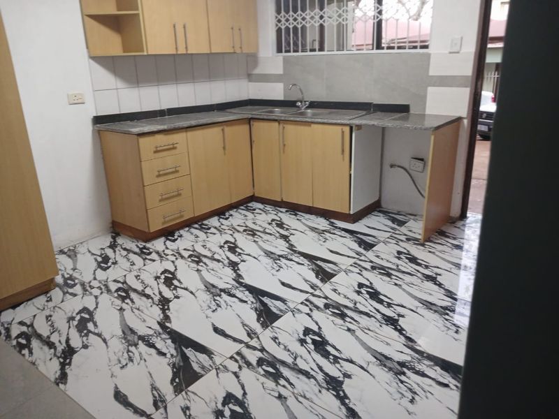A functional kitchen featuring light wood cabinetry, granite countertops, and striking marble-effect floor tiles, offering a clean and modern aesthetic.