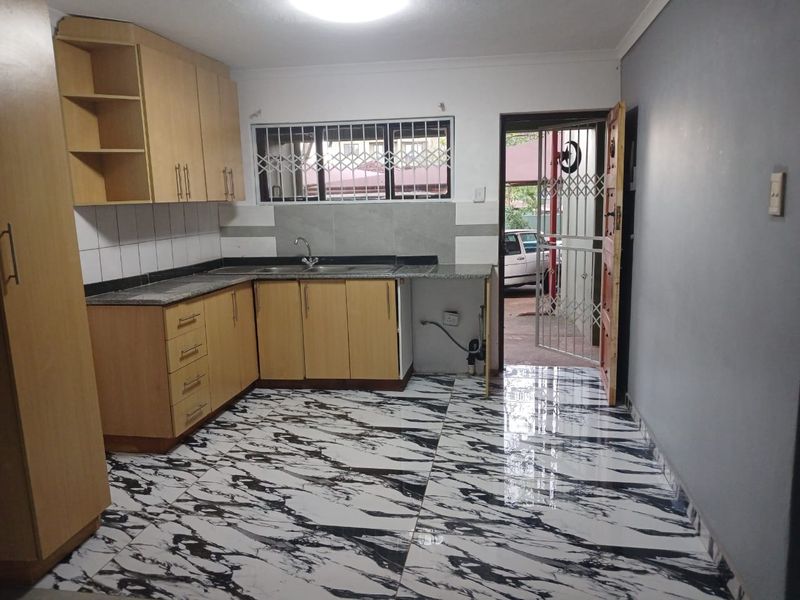 A functional kitchen featuring light wood cabinetry, granite countertops, and bold marble-patterned floor tiles, with direct access to an exterior entrance.