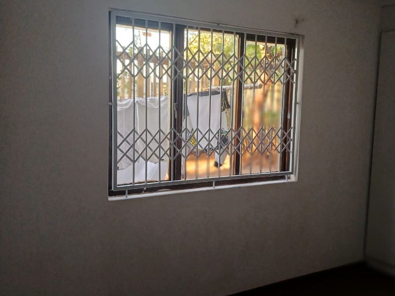 An empty bedroom featuring a window with a fitted security gate, providing a blank canvas for potential interior design and renovation.