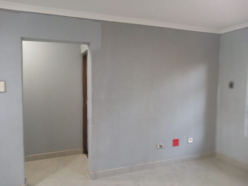 An empty living room area featuring neutral grey walls, coving, and tiled flooring, ready for personalization and furniture placement.