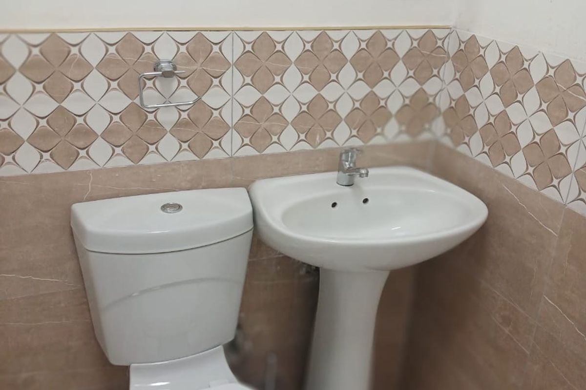 A compact bathroom featuring a white pedestal washbasin, a standard toilet, and decorative patterned wall tiling.
