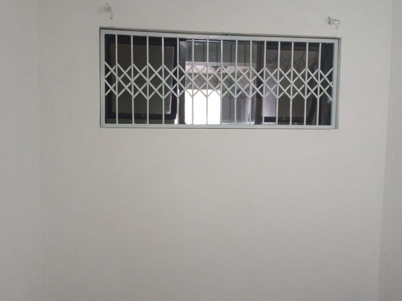 An empty bedroom featuring carpet flooring and a window fitted with a white security gate.