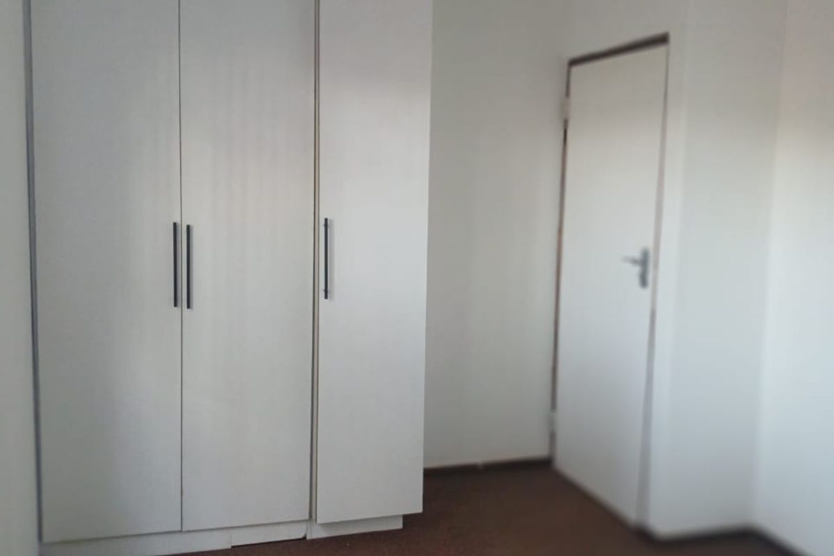 An empty bedroom featuring built-in white cupboards and carpeted flooring, requiring minor cosmetic updates to improve the overall finish.