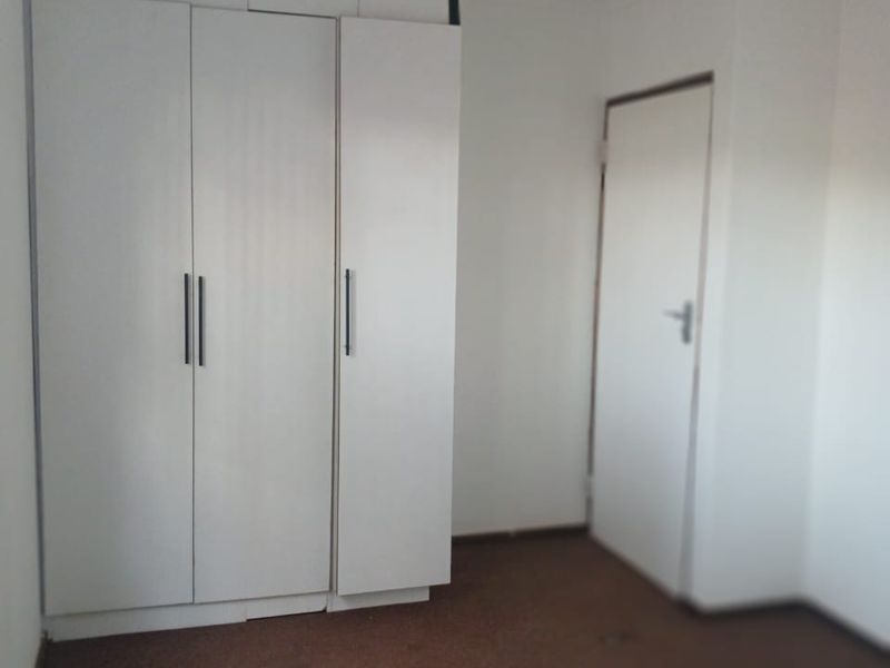 An empty bedroom featuring built-in white cupboards and carpeted flooring, requiring minor cosmetic updates to improve the overall finish.