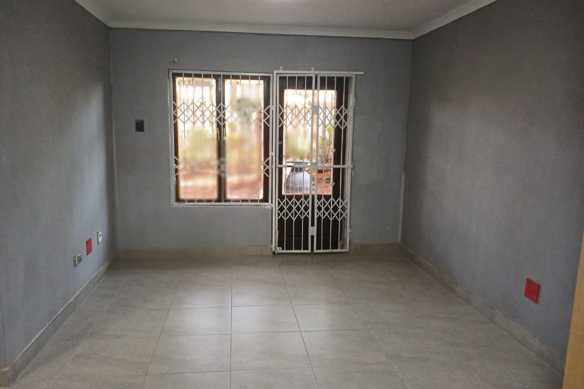 An empty living room featuring grey painted walls, tiled flooring, and secure window and door access with fitted security gates.
