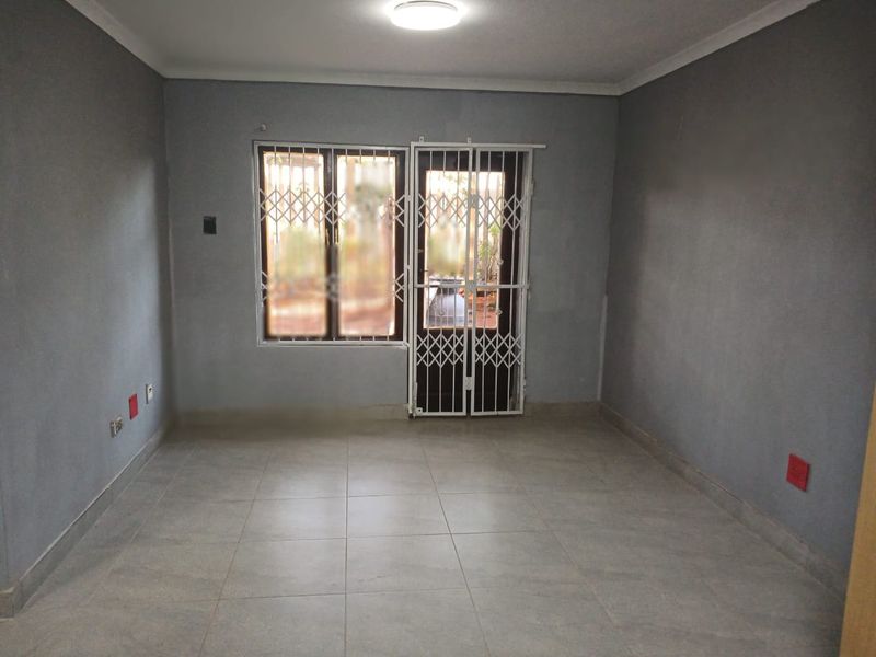 An empty living room featuring grey painted walls, tiled flooring, and secure window and door access with fitted security gates.