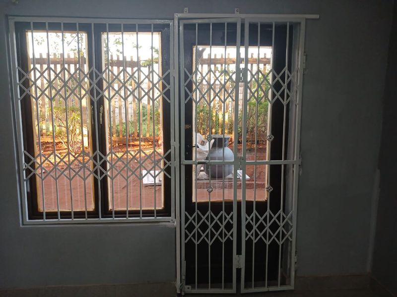 An interior view of a room featuring a timber frame window and door, both fitted with white security gates for added protection.
