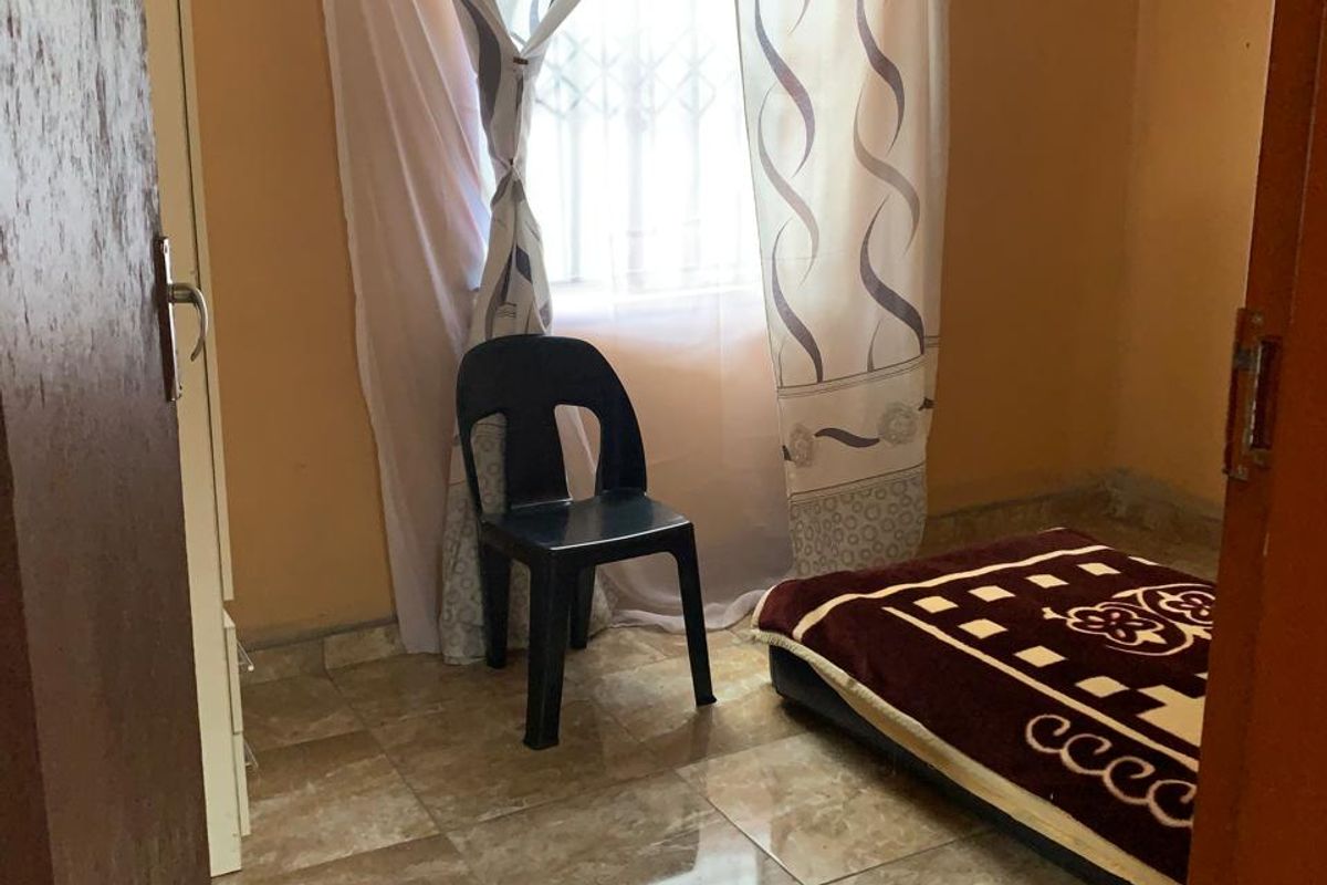 A compact bedroom featuring tiled flooring, a window with security bars, and a built-in cupboard, offering a functional space for rest.