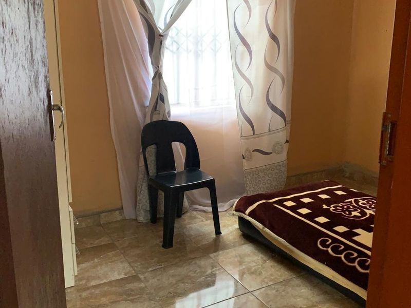 A compact bedroom featuring tiled flooring, a window with security bars, and a built-in cupboard, offering a functional space for rest.
