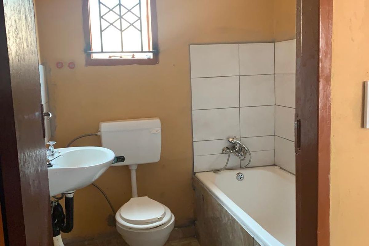 A compact bathroom featuring a bathtub, pedestal basin, and toilet, with tiled splashbacks and a security-grille window. Requires cosmetic updates.