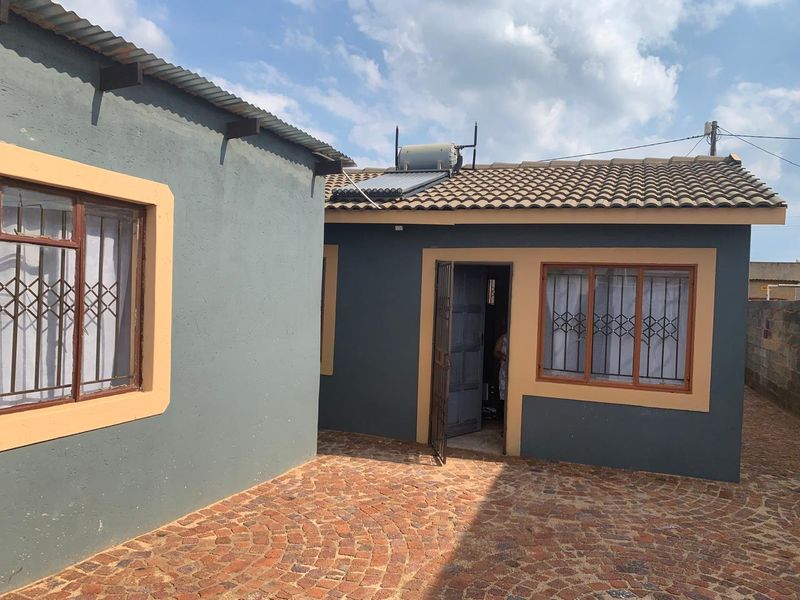 Rear exterior view of the property featuring a paved courtyard, solar water heating system, and secure window grilles.