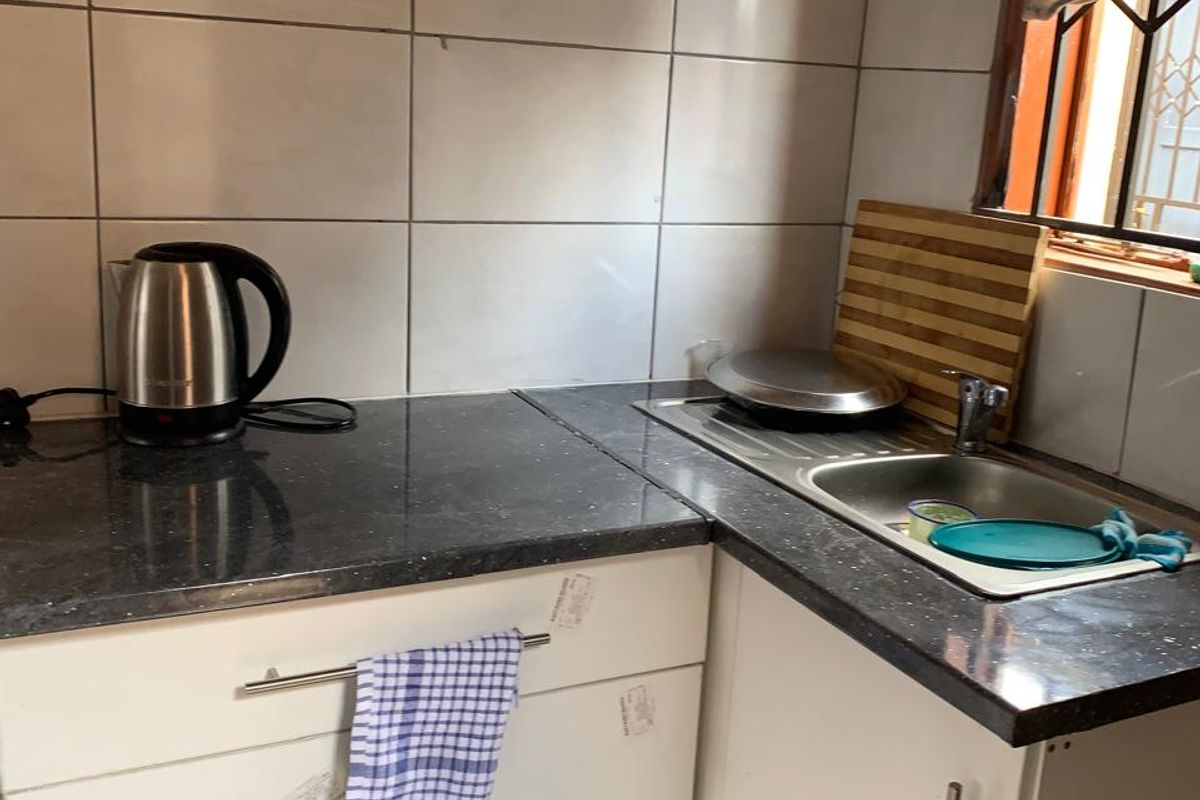 A compact kitchen area featuring white cabinetry, dark laminate countertops, and a stainless steel sink with tiled splashback.
