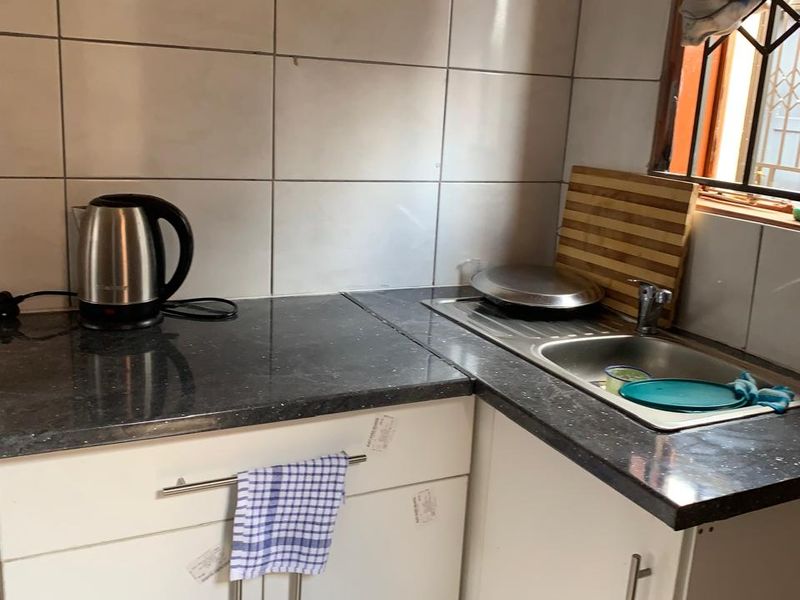 A compact kitchen area featuring white cabinetry, dark laminate countertops, and a stainless steel sink with tiled splashback.