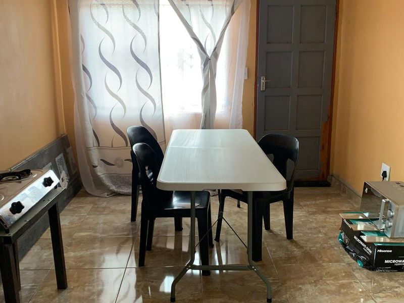 A simple dining area featuring tiled flooring and a panel door, offering a functional space that could benefit from cosmetic updates.