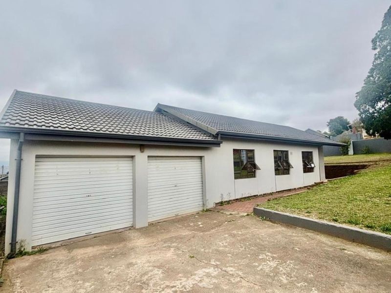 Exterior view of the property featuring a double garage, tiled roof, and concrete driveway with adjacent lawn area.