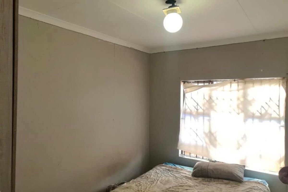 A bedroom featuring security bars on the window and simple ceiling lighting, requiring cosmetic updates to the wall finishes.
