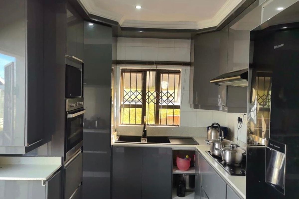 Modern kitchen featuring high-gloss grey cabinetry, integrated appliances, built-in oven and microwave, and a double sink with security bars on the window.