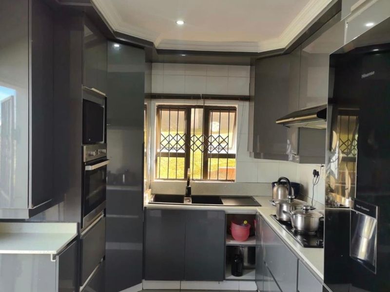 Modern kitchen featuring high-gloss grey cabinetry, integrated appliances, built-in oven and microwave, and a double sink with security bars on the window.