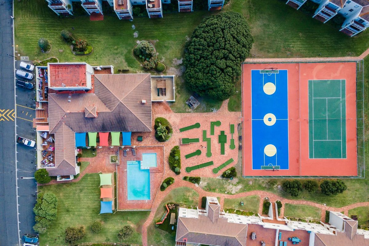 Aerial view of the apartment complex featuring a swimming pool, tennis court, basketball court, mini golf course, and well-maintained landscaped grounds.