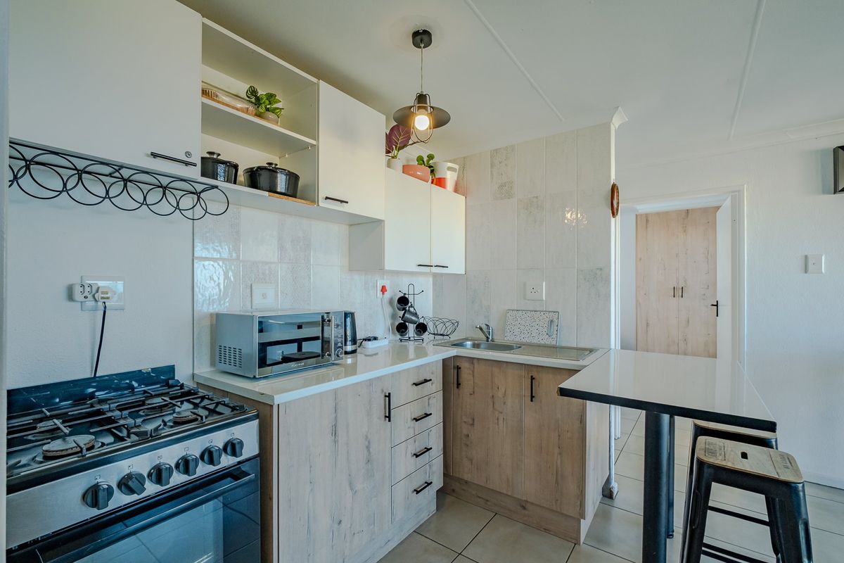 Compact modern kitchen featuring light wood-finish cabinetry, a gas stove, stainless steel sink, and a convenient breakfast bar area.