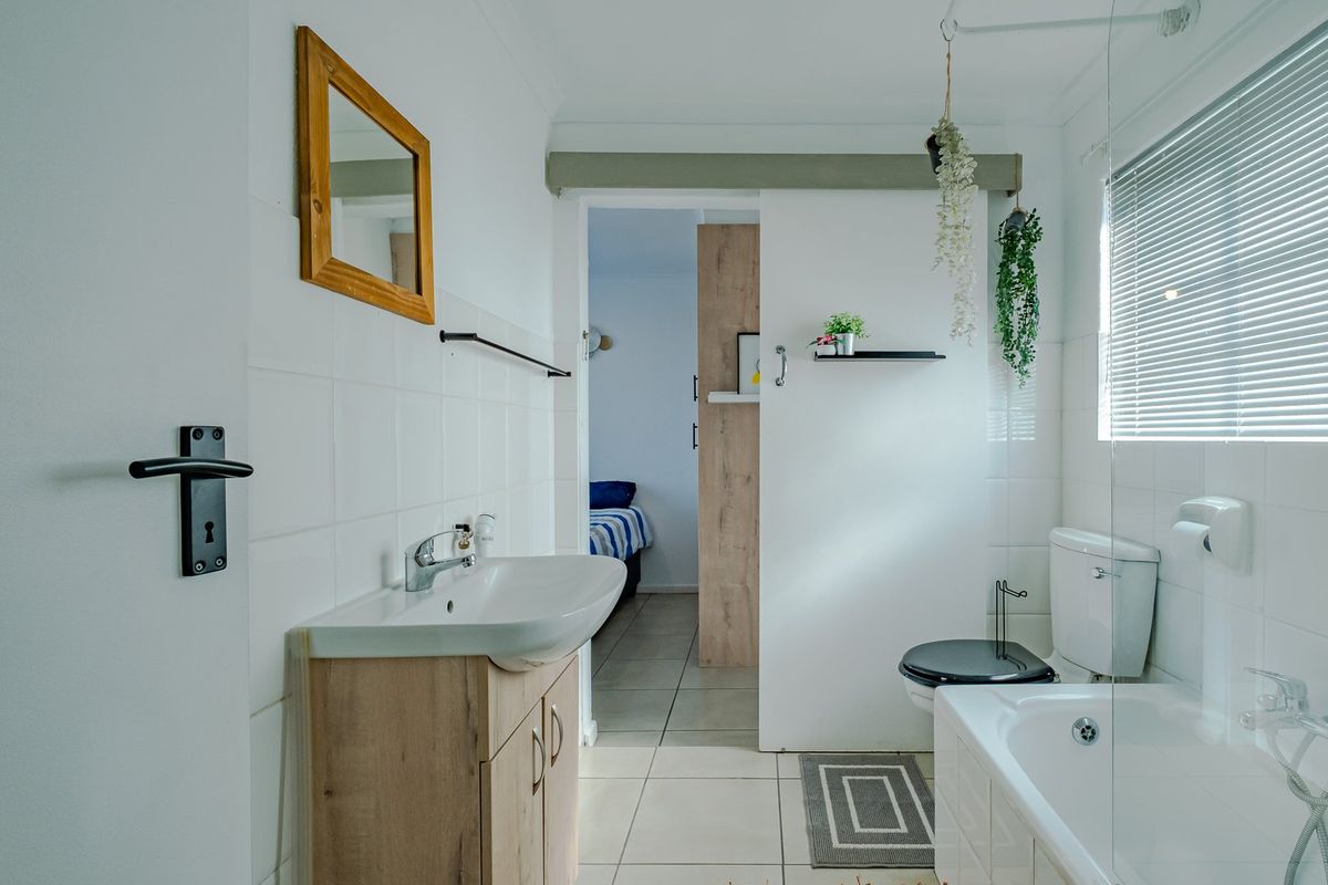 A clean and functional bathroom featuring a vanity unit, bathtub with glass screen, and a sliding door leading to the adjacent bedroom.
