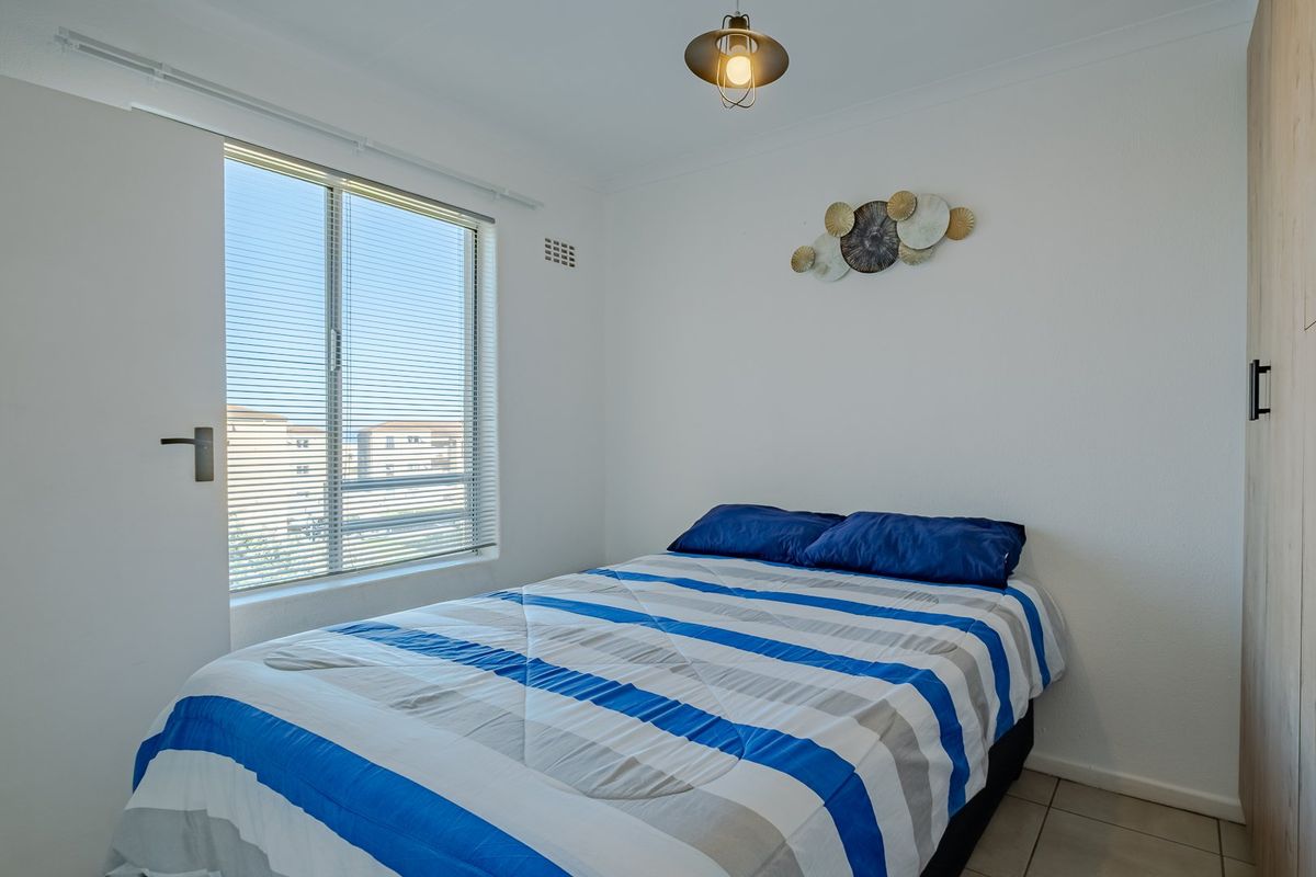 A bright bedroom featuring tiled flooring, a built-in wardrobe, and a window fitted with venetian blinds.