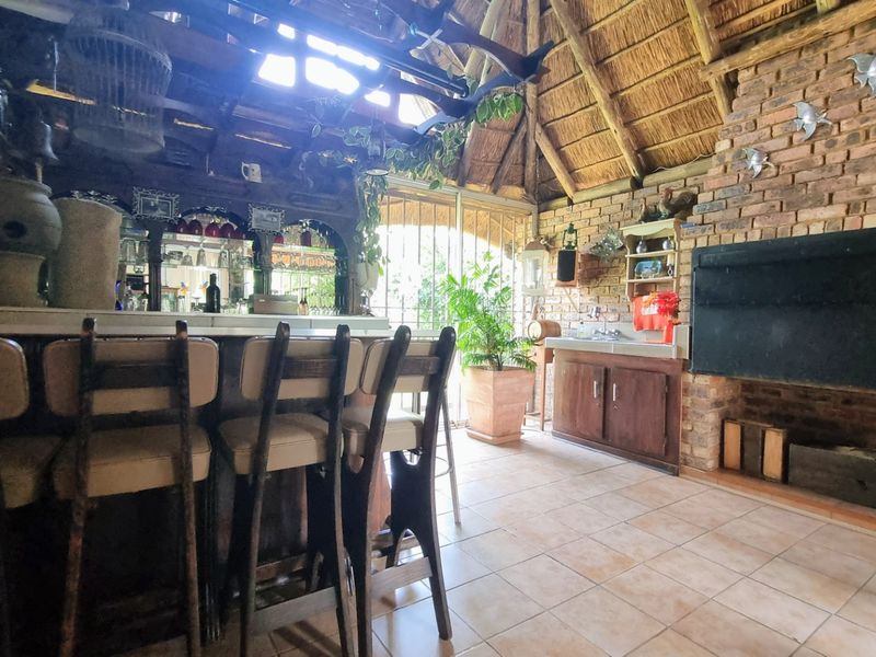 Rustic entertainment area featuring a built-in bar, exposed brick walls, a large fireplace, and a traditional thatched roof with tiled flooring.