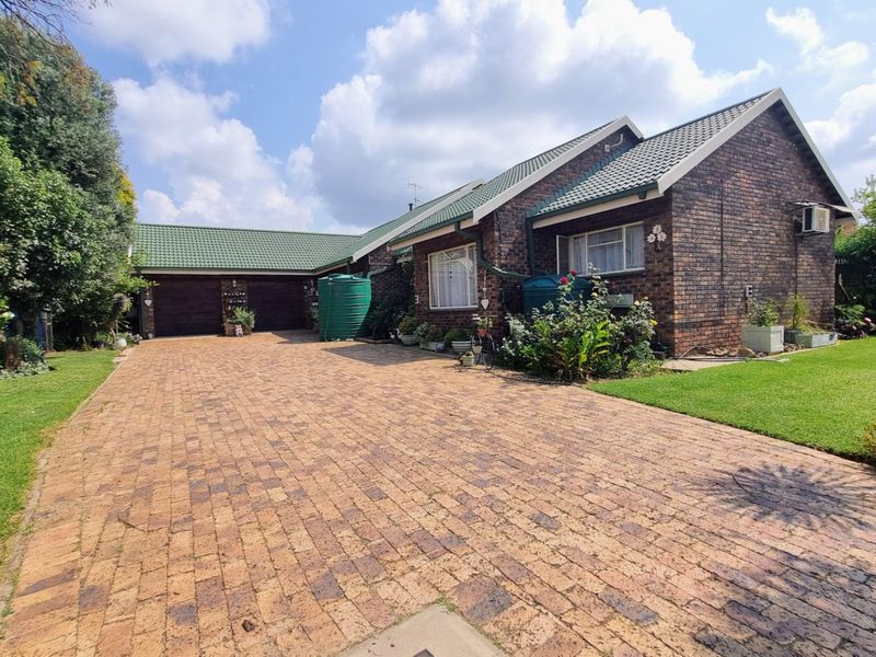 Front exterior view of a brick house featuring a large paved driveway, green tiled roof, and established garden surroundings.