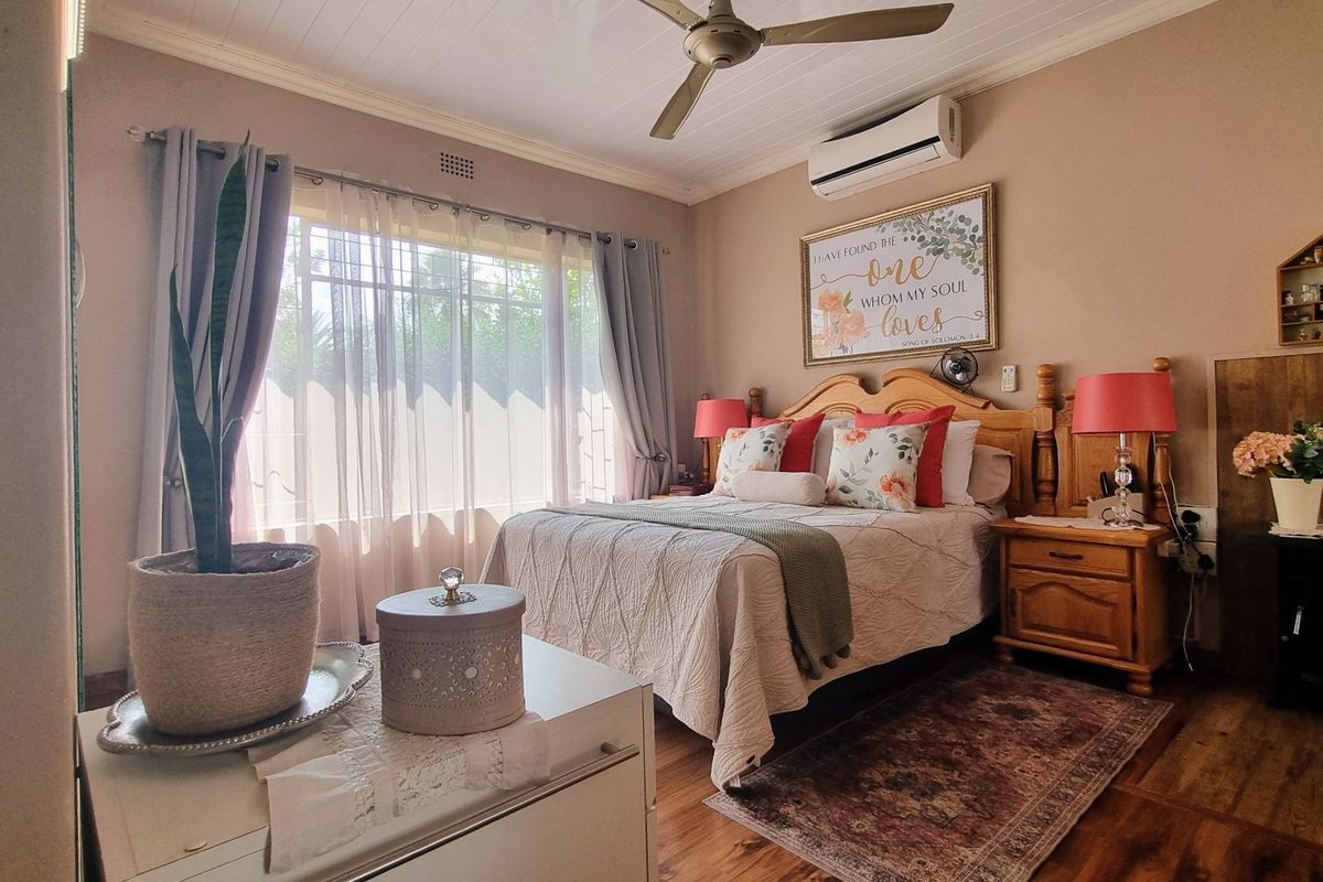 A well-maintained bedroom featuring timber flooring, a ceiling fan, and a wall-mounted split-system air conditioner for climate control.